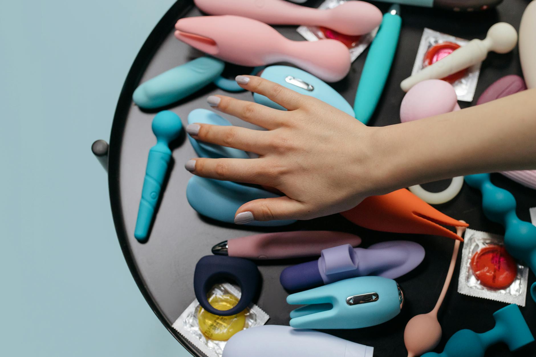 A hand reaching over a variety of colorful clitoral vibrators arranged on a table, ready for exploration.
