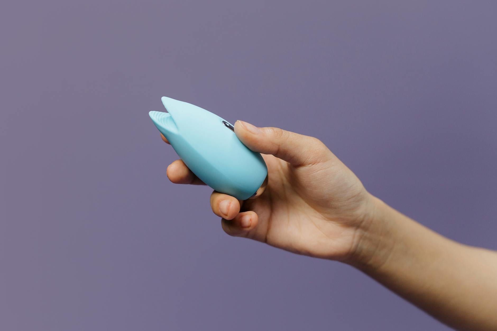 A blue silicone vibrator held in hand against a solid purple background, promoting self-love and sexuality